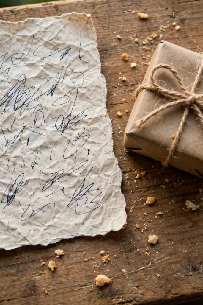Close-up of a handwritten thank-you note on paper next to a small gift box on a wooden table